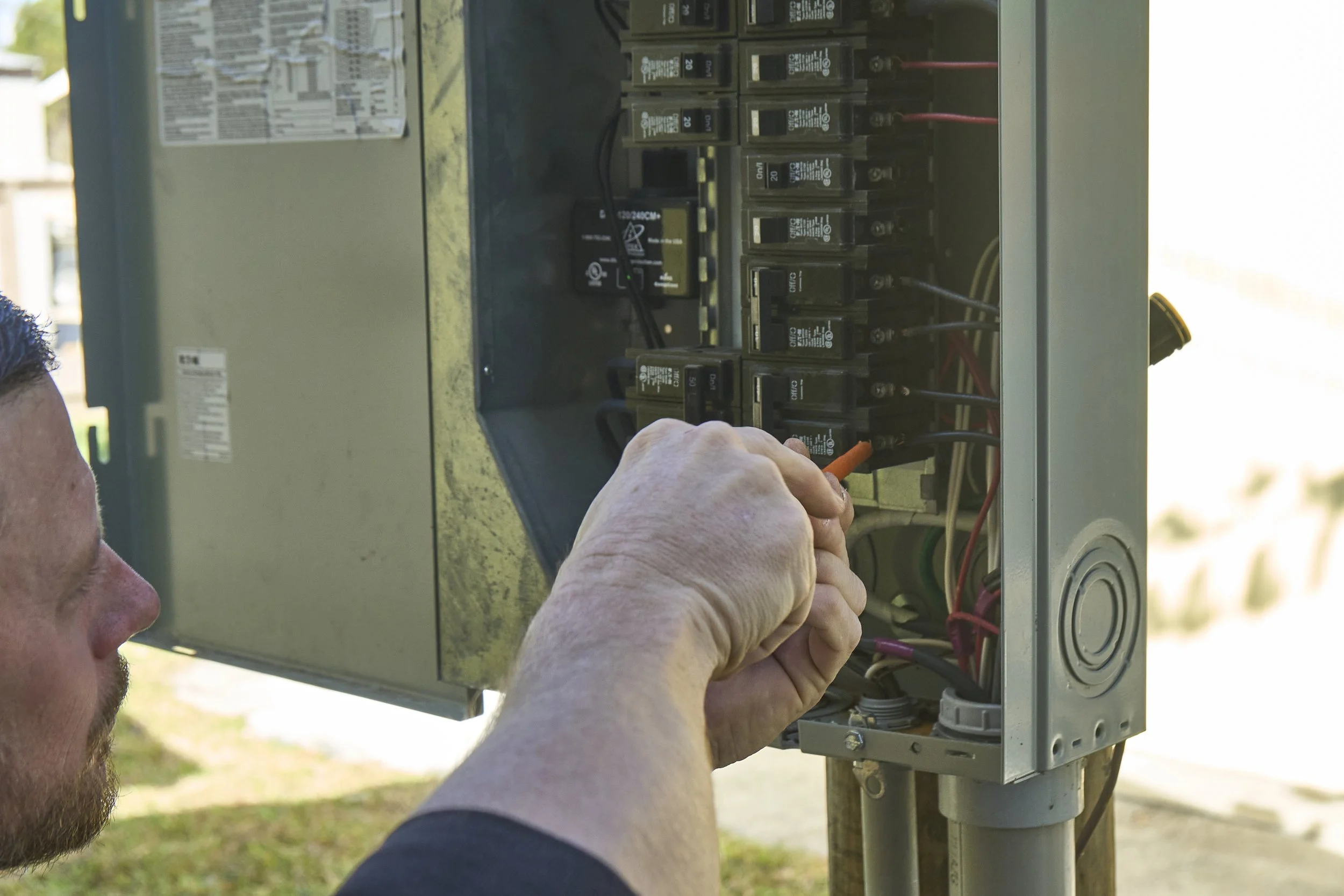 Hand reaching into an open exterior breaker/meter panel