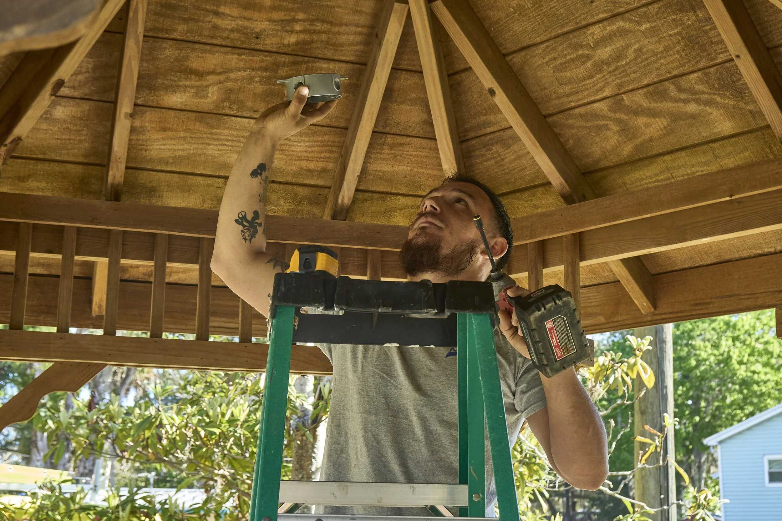 Man on a ladder installing a fixture under a wood gazebo ceiling