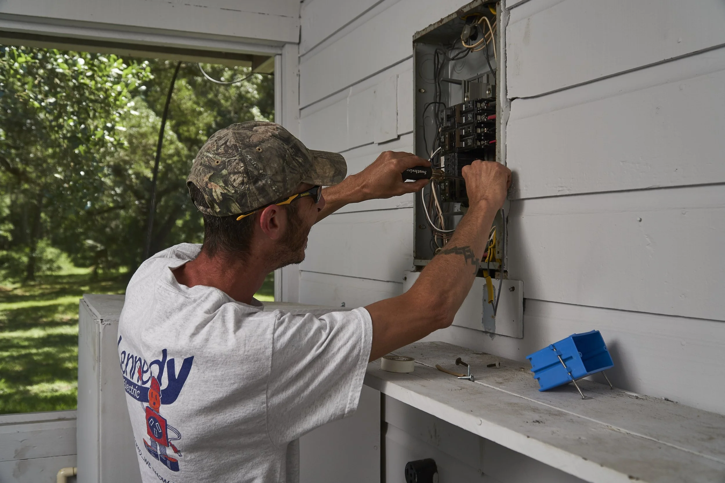 Electrician at an open panel on an exterior porch wall (front view)