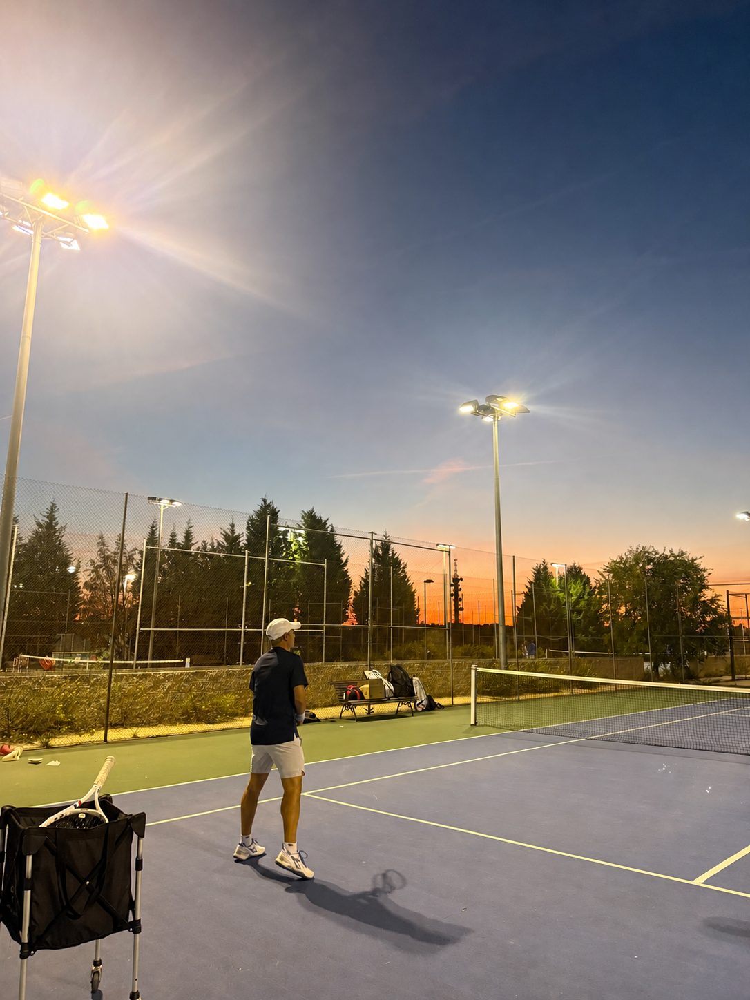 Enzo Bicchieri practising tennis on a hard court at dusk