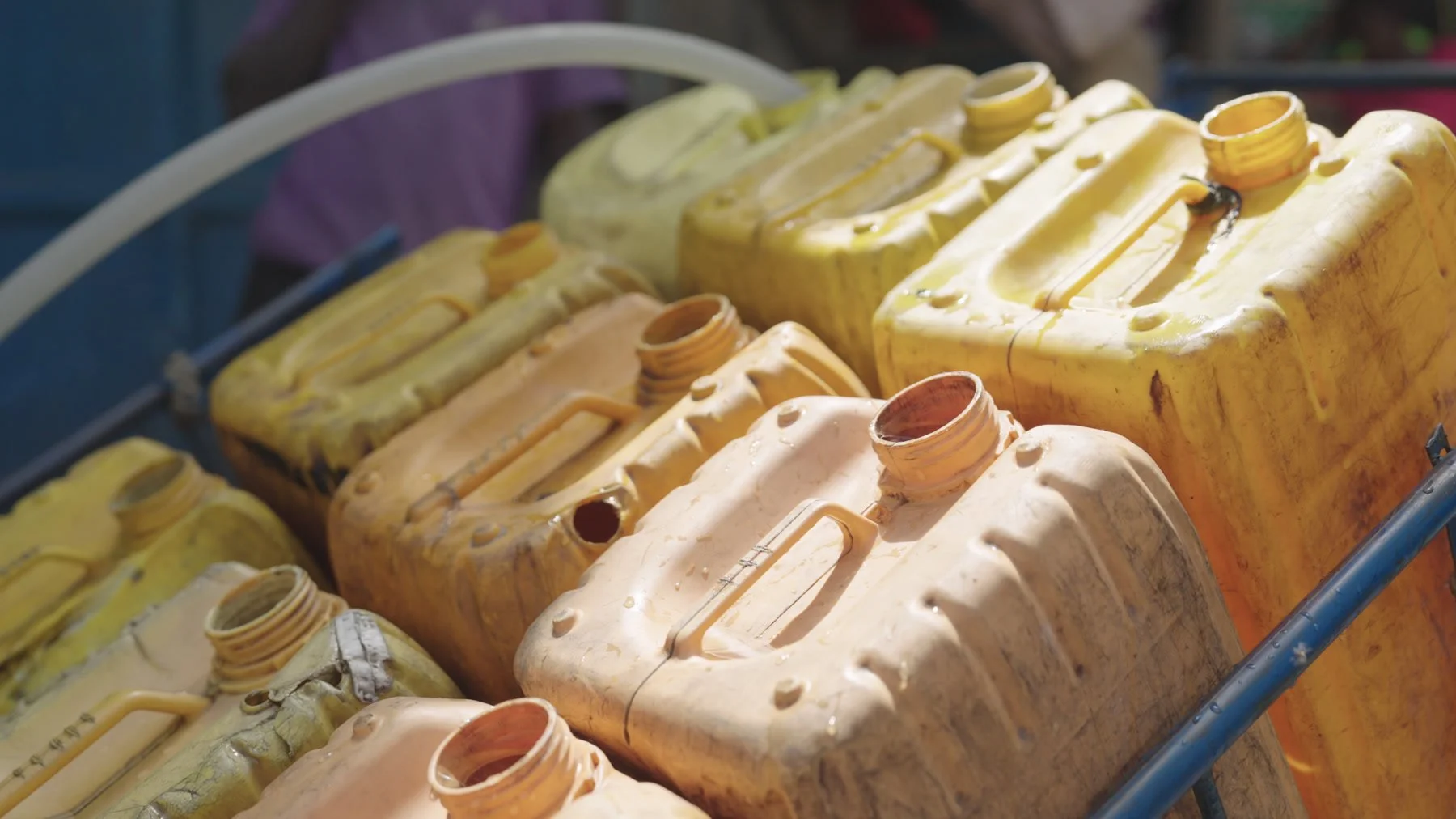 Worn, stained yellow jerrycans with open necks grouped on a cart in Nairobi.