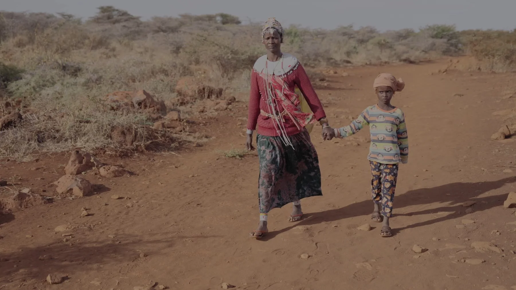A mother and daughter carry yellow jerrycans through the dry Marsabit landscape.
