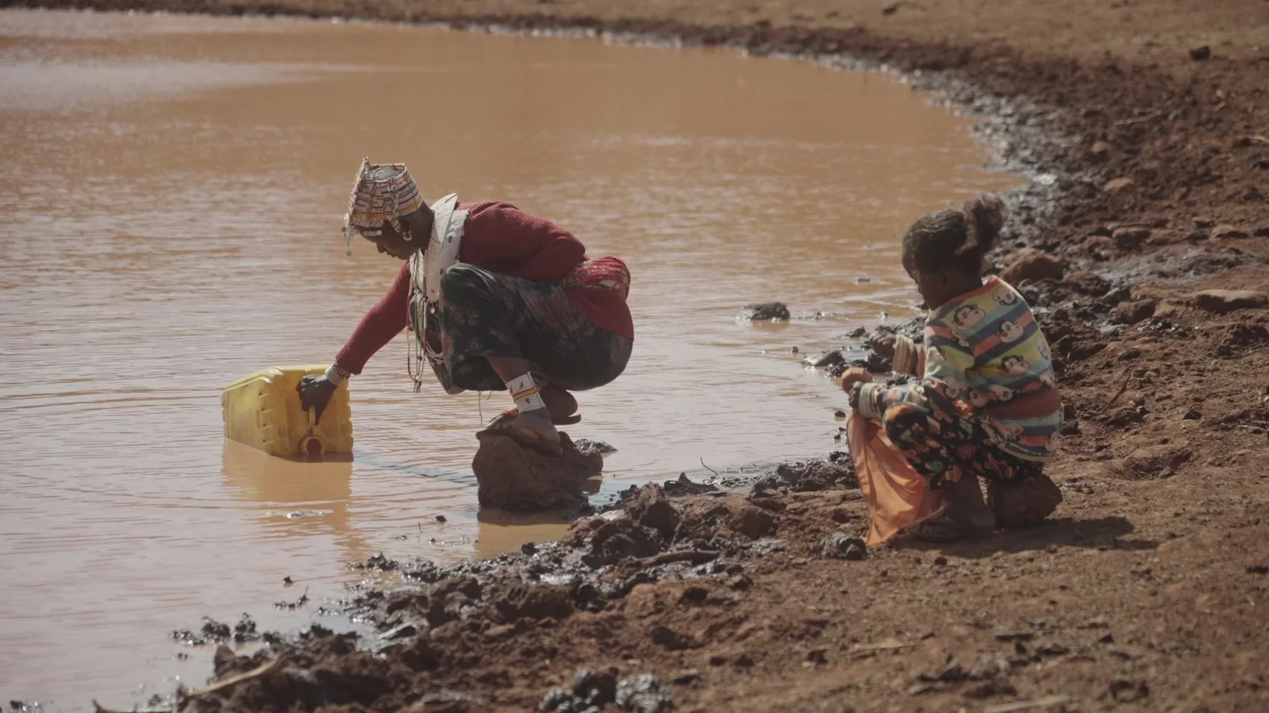 A woman fills a yellow jerrycan at a water source.