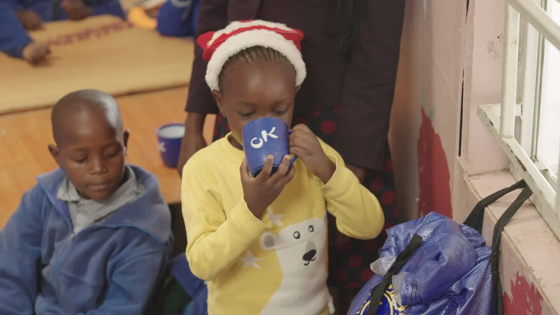 A child drinks from a blue cup beside a WaterSafe hanging at her classroom window.