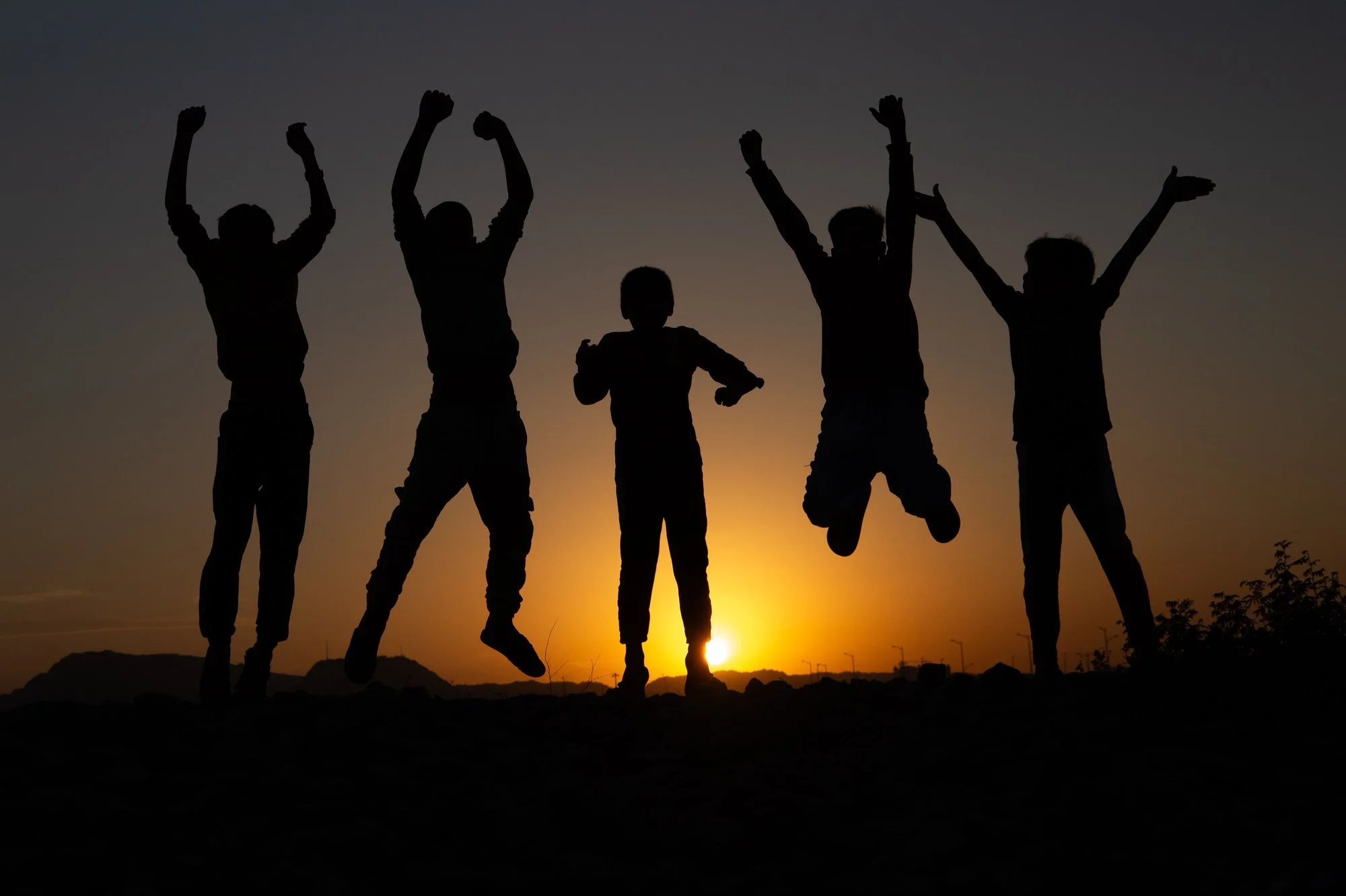 Five children jumping with their arms raised, silhouetted against a sunset