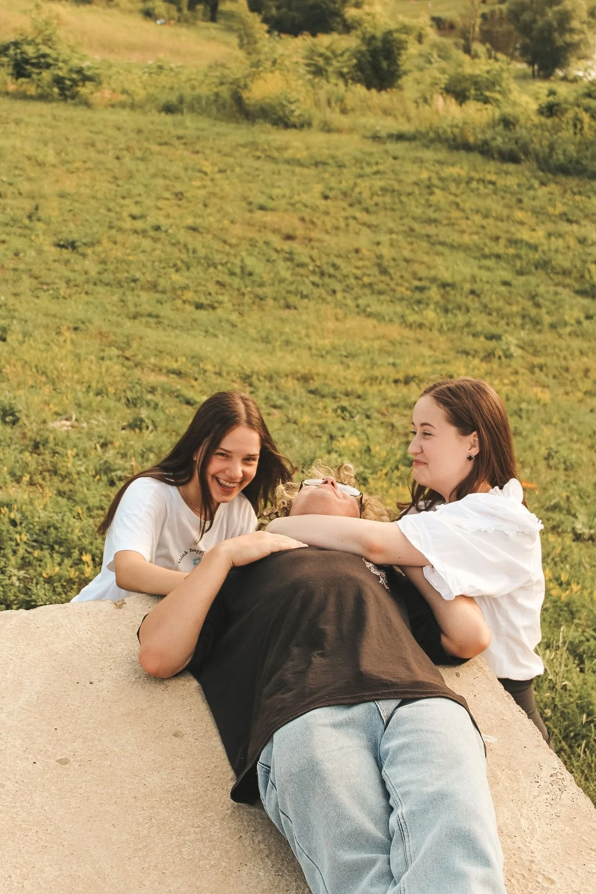 Three young friends laughing together on a sunny hillside