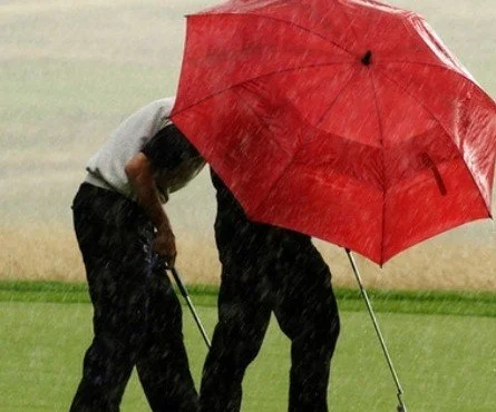 Golfers sharing a red umbrella