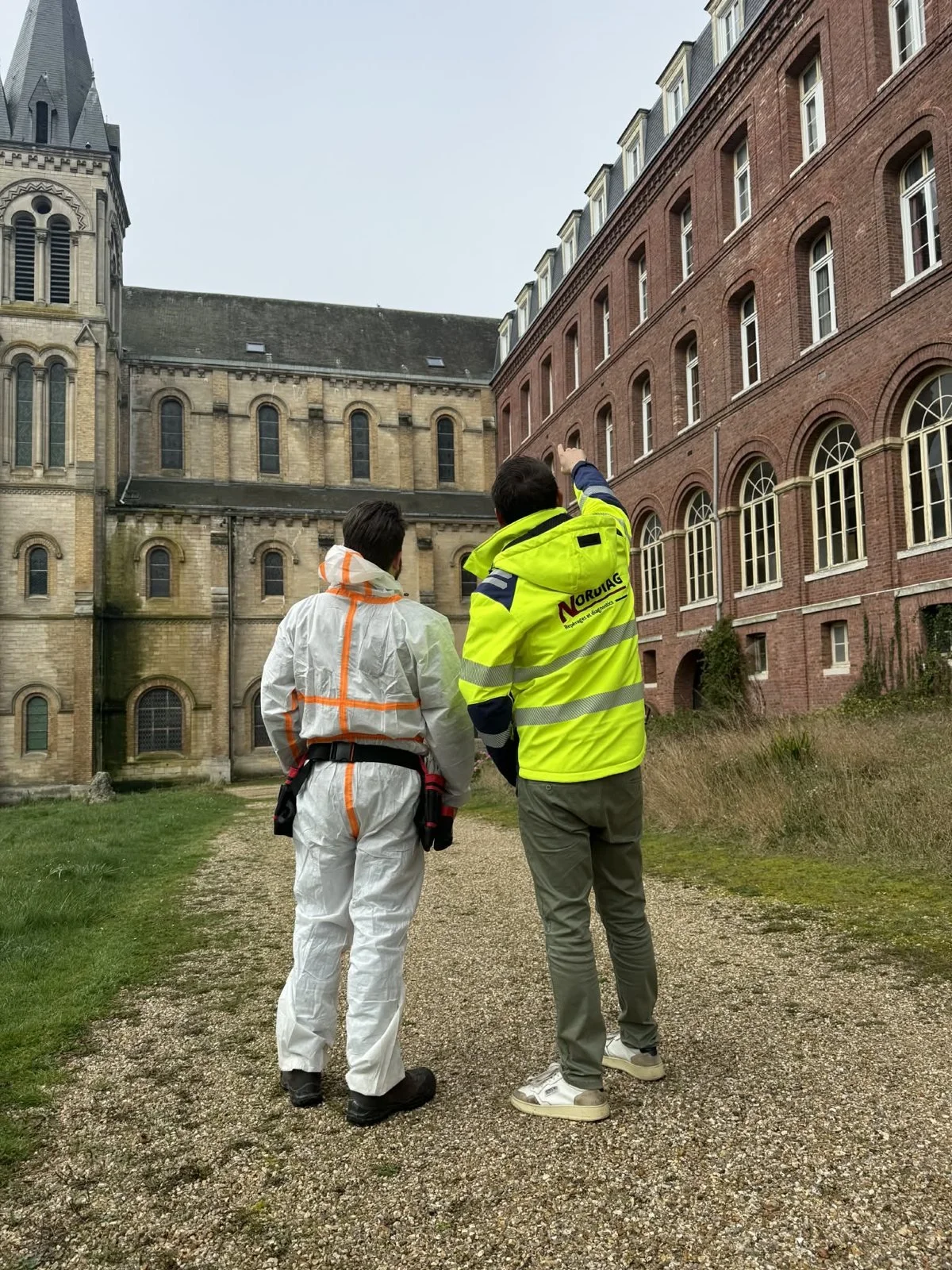 Deux diagnostiqueurs NORDIAG, l’un en combinaison de protection, observent un bâtiment ancien avant un repérage amiante