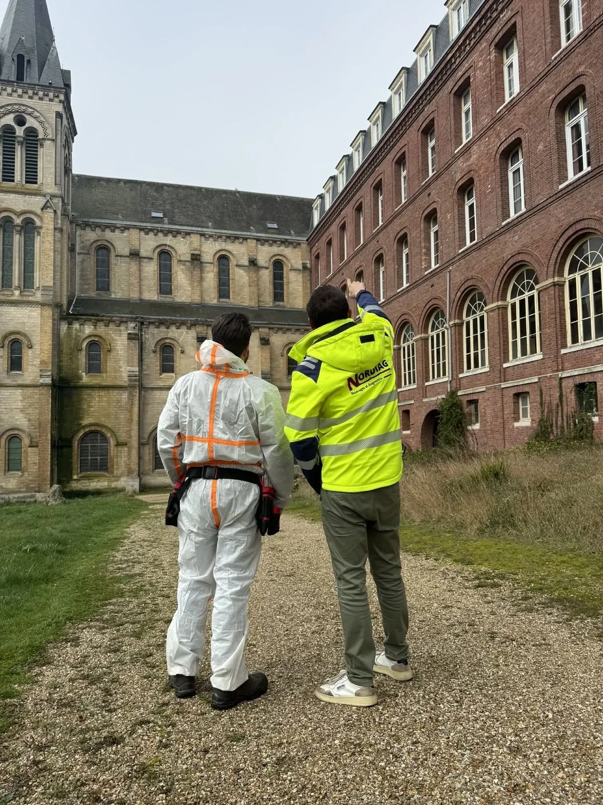 Repérage avant travaux devant un bâtiment ancien à réhabiliter, en combinaison de protection et veste NORDIAG