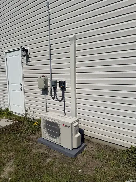 Outdoor Mitsubishi mini-split with a covered refrigerant line and equipment pad