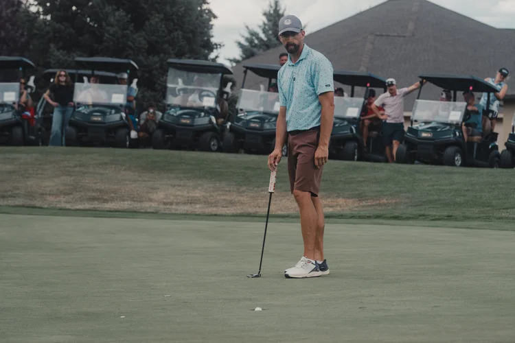 A golfer stands with a putter near the clubhouse.