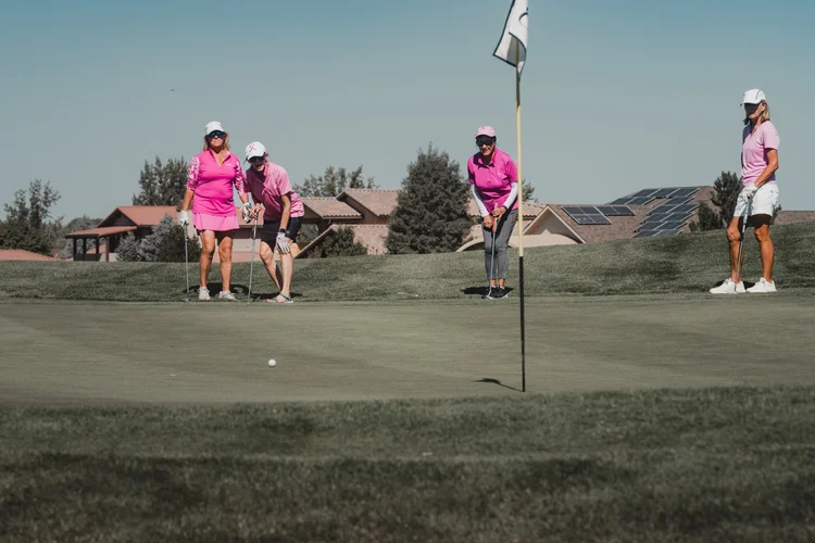 Players in pink watch a putt near the flagstick.
