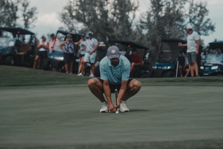 A player crouches to read a putt, with spectators behind.