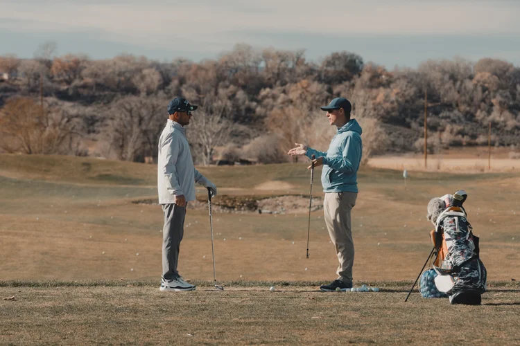 Two golfers talk beside a golf bag on a winter fairway.