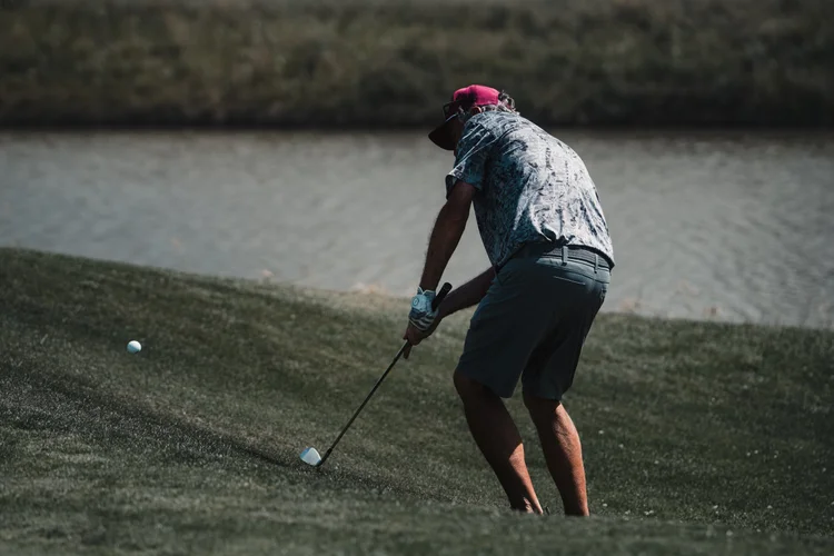 A golfer plays an approach beside the water.
