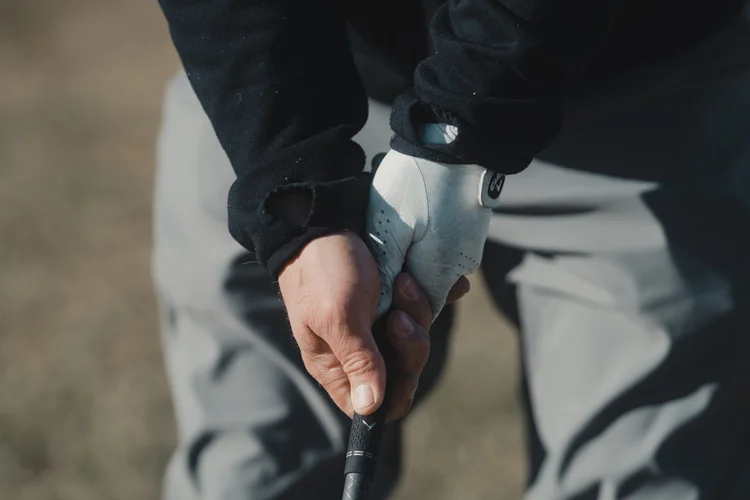 A close view of a golfer gripping a club with bare and gloved hands.