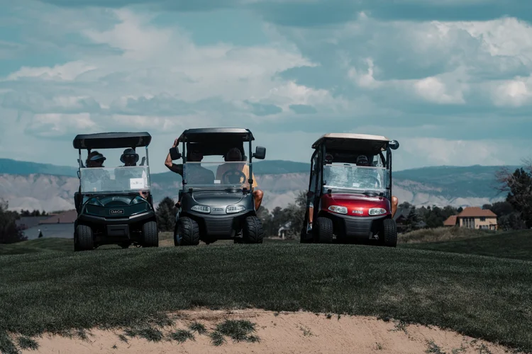 Three golf carts wait beside a bunker, with mountains in the distance.