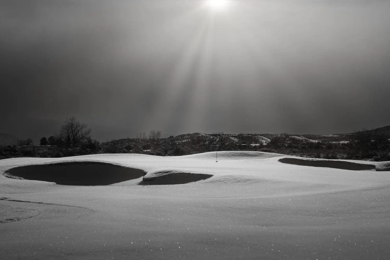 Sunlight over snow-covered bunkers, photographed in black and white.
