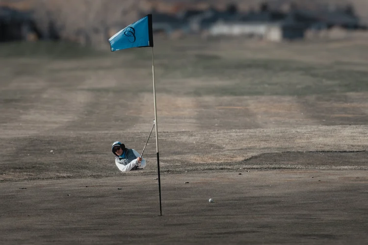 A blue flag and a golfer on a dormant putting green.