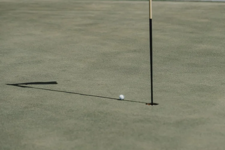 A golf ball rests near the flagstick and its shadow.