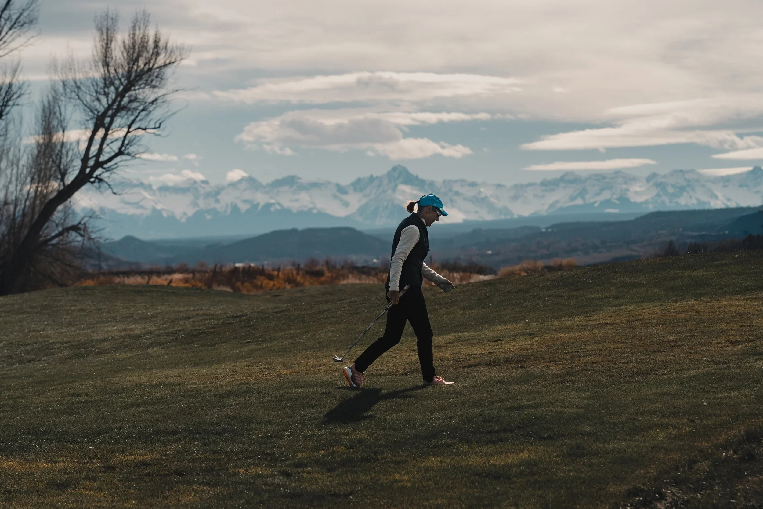 A golfer walking across a winter fairway beneath the Colorado mountains.