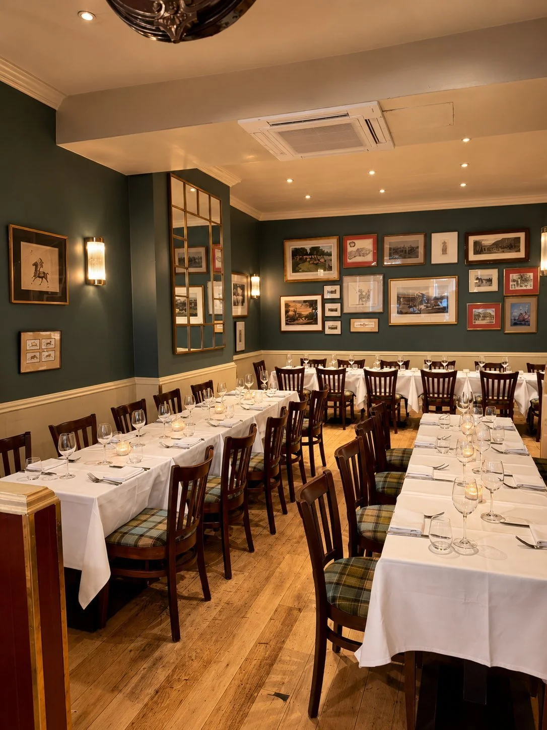 The dining room laid for a private party: long tables with white cloths and candles, tartan chairs, green walls hung with framed prints