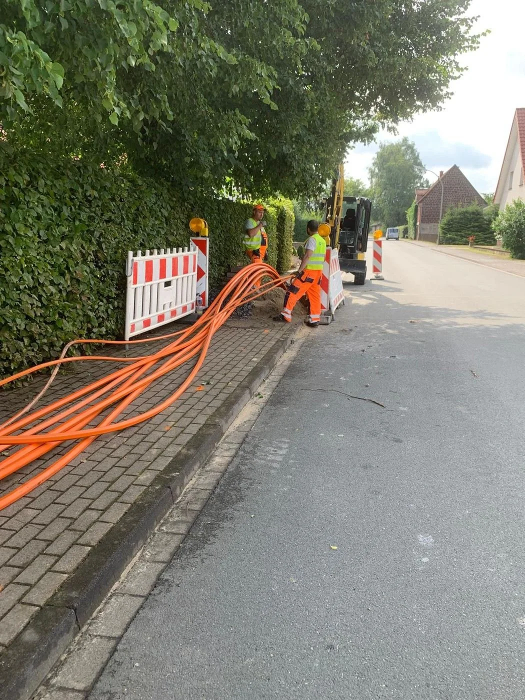 Zwei Mitarbeiter ziehen orange Schutzrohre in den Graben ein, Lichtenau