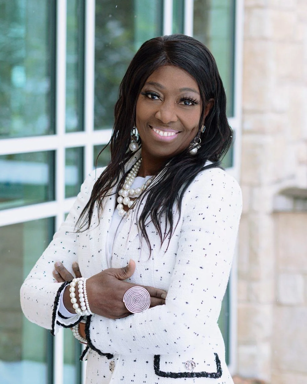 Nana Noi, Global Realtor, in a white tweed jacket, smiling, arms folded