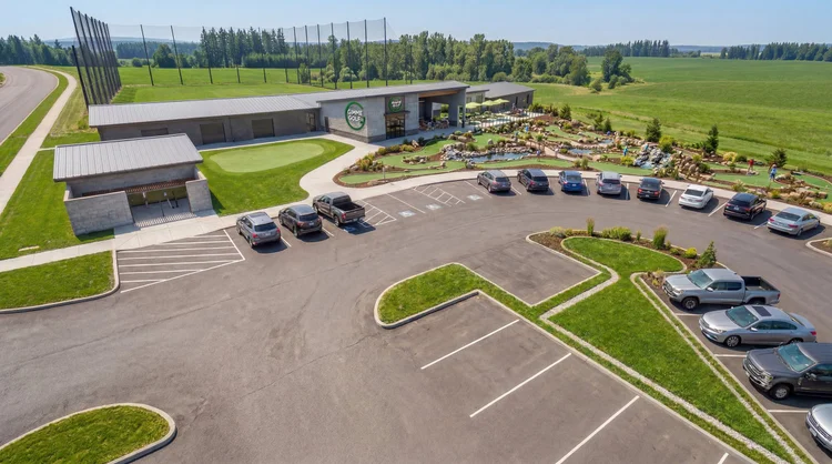Gimme Golf front entry and clubhouse seen from above the parking lot, with the range behind