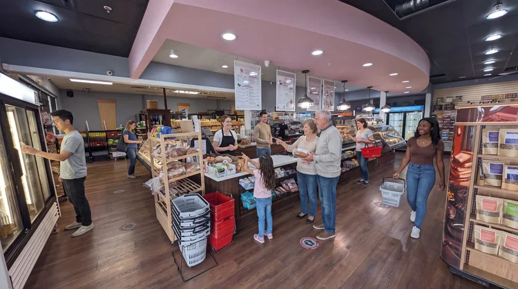 Love & Appetite market floor with the bakery counter, deli case and shoppers under a curved pink soffit