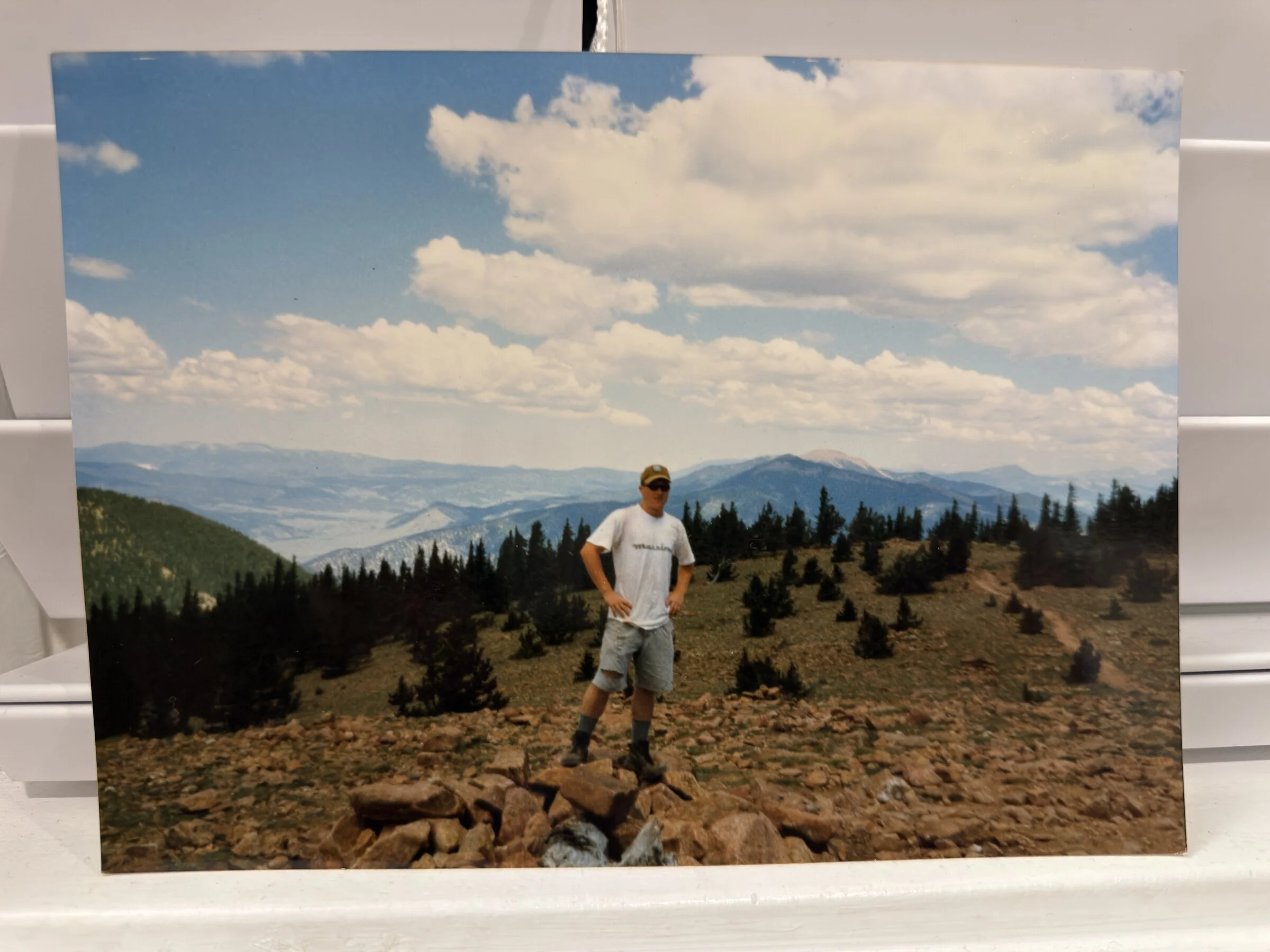 Mike as a young Scout standing on a rocky summit near treeline, mountains and big clouds behind