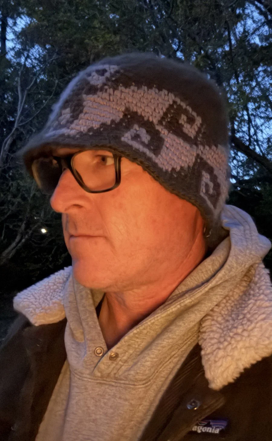 Mike at dusk in a knit hat and sherpa-collared jacket, looking off toward the trees