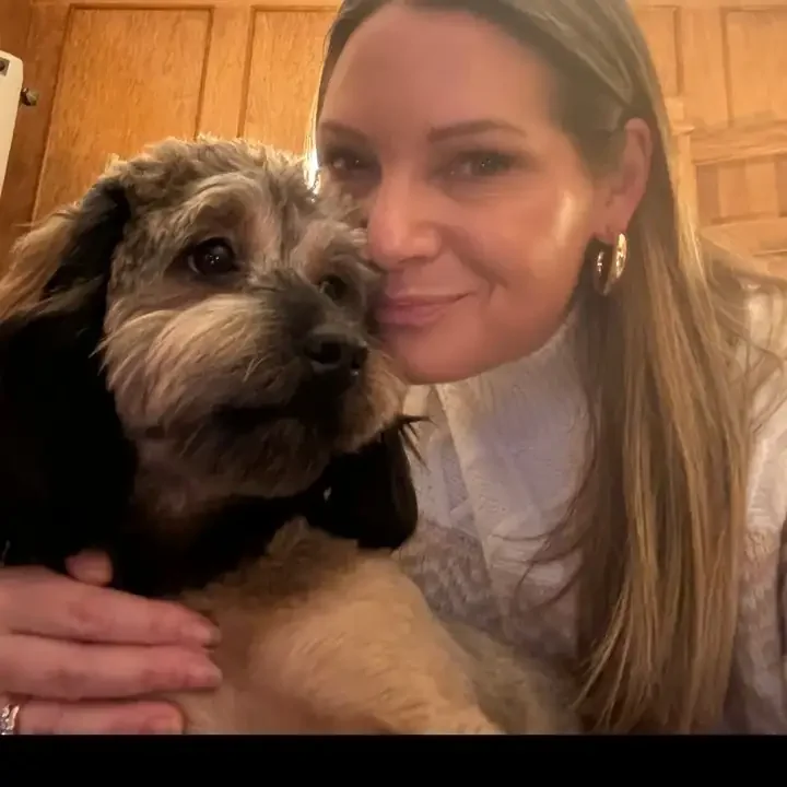 Kim Webber smiling, cheek to cheek with her scruffy dog