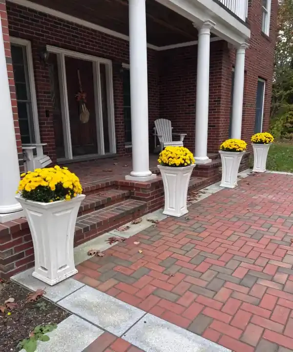 The front porch of Kim's brick house, with white columns, two Adirondack chairs and planters of yellow mums