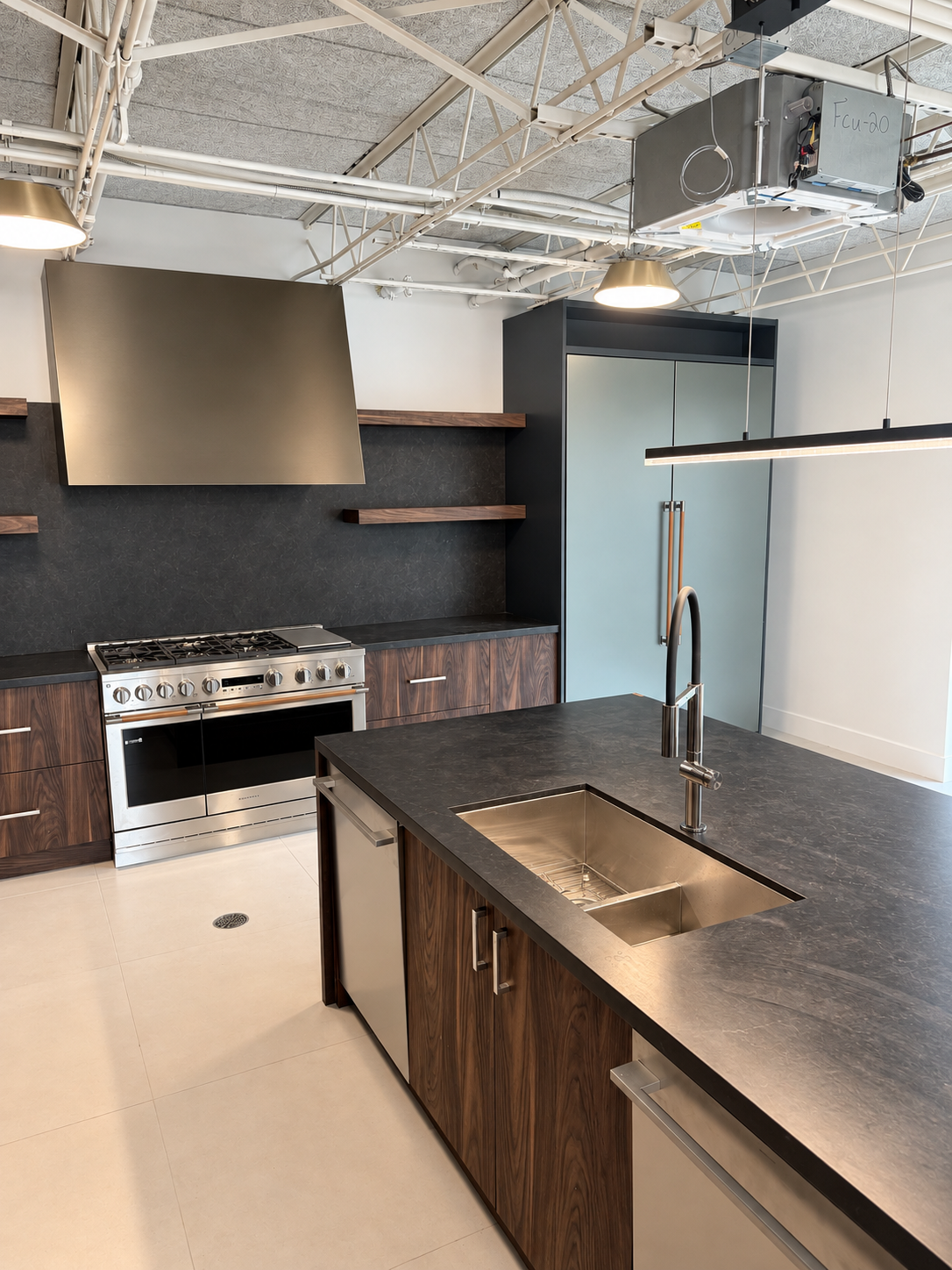 Dark wood cabinetry, a bronze range hood and a stone island in a TLTH showroom kitchen.