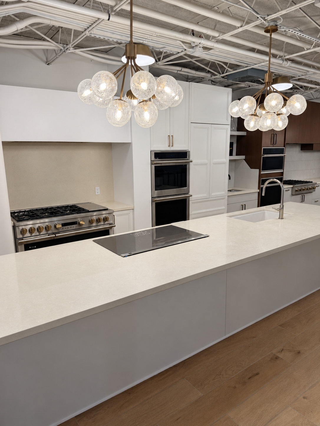 A white kitchen with induction island, sink and globe chandeliers at The Luxury Tree House showroom.