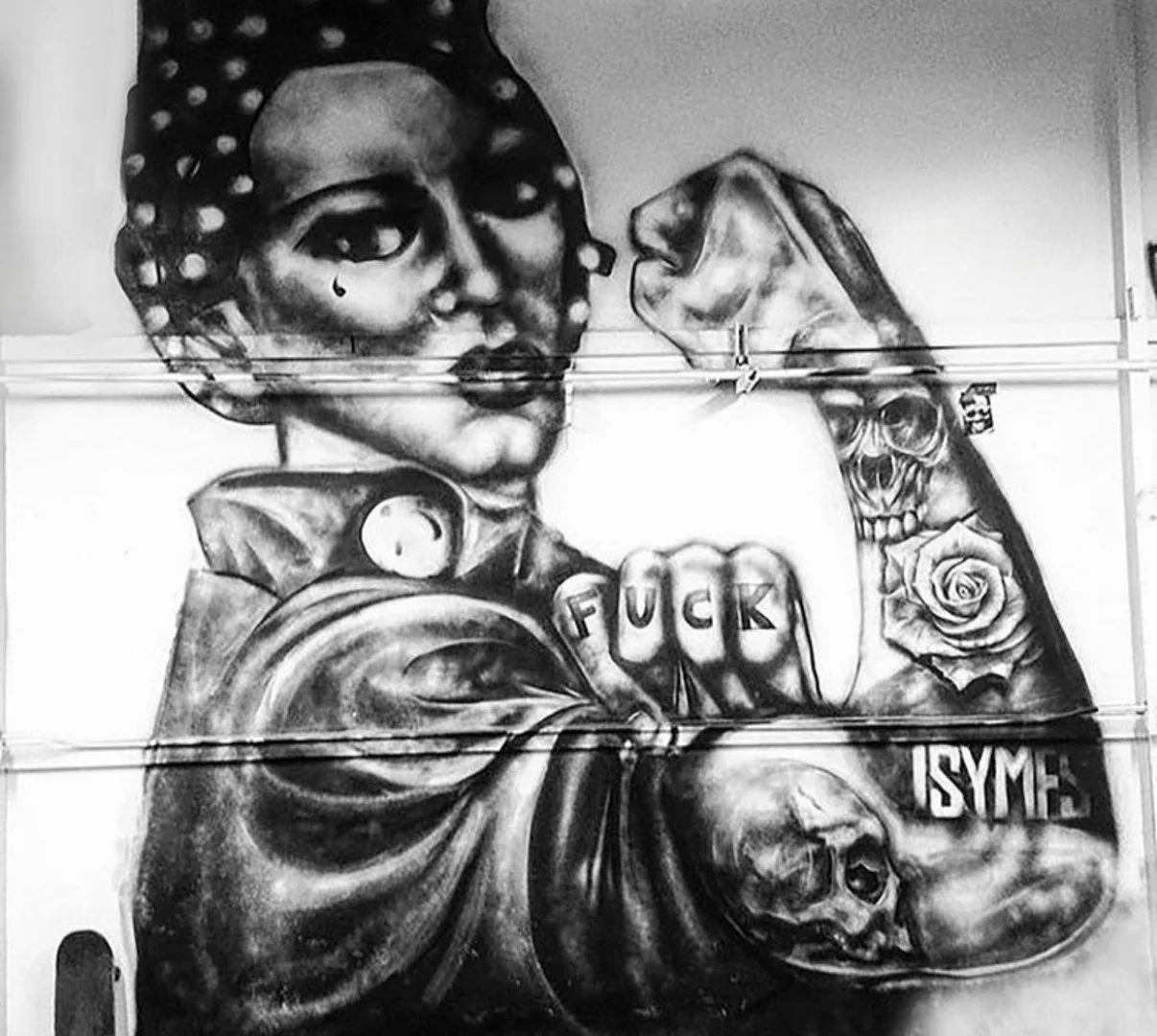 Black and white mural of a woman with a raised fist, roses and skull details