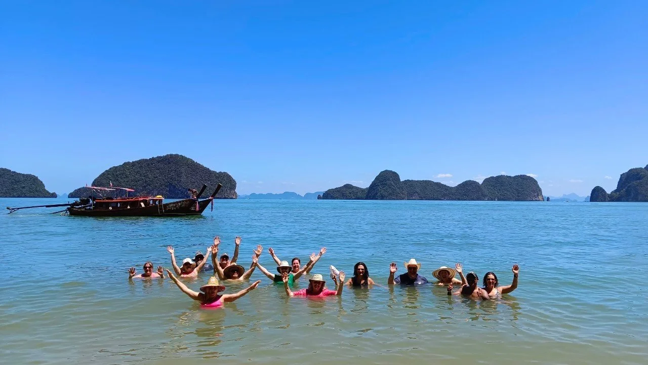 Our group swimming beside a longtail boat in a turquoise bay