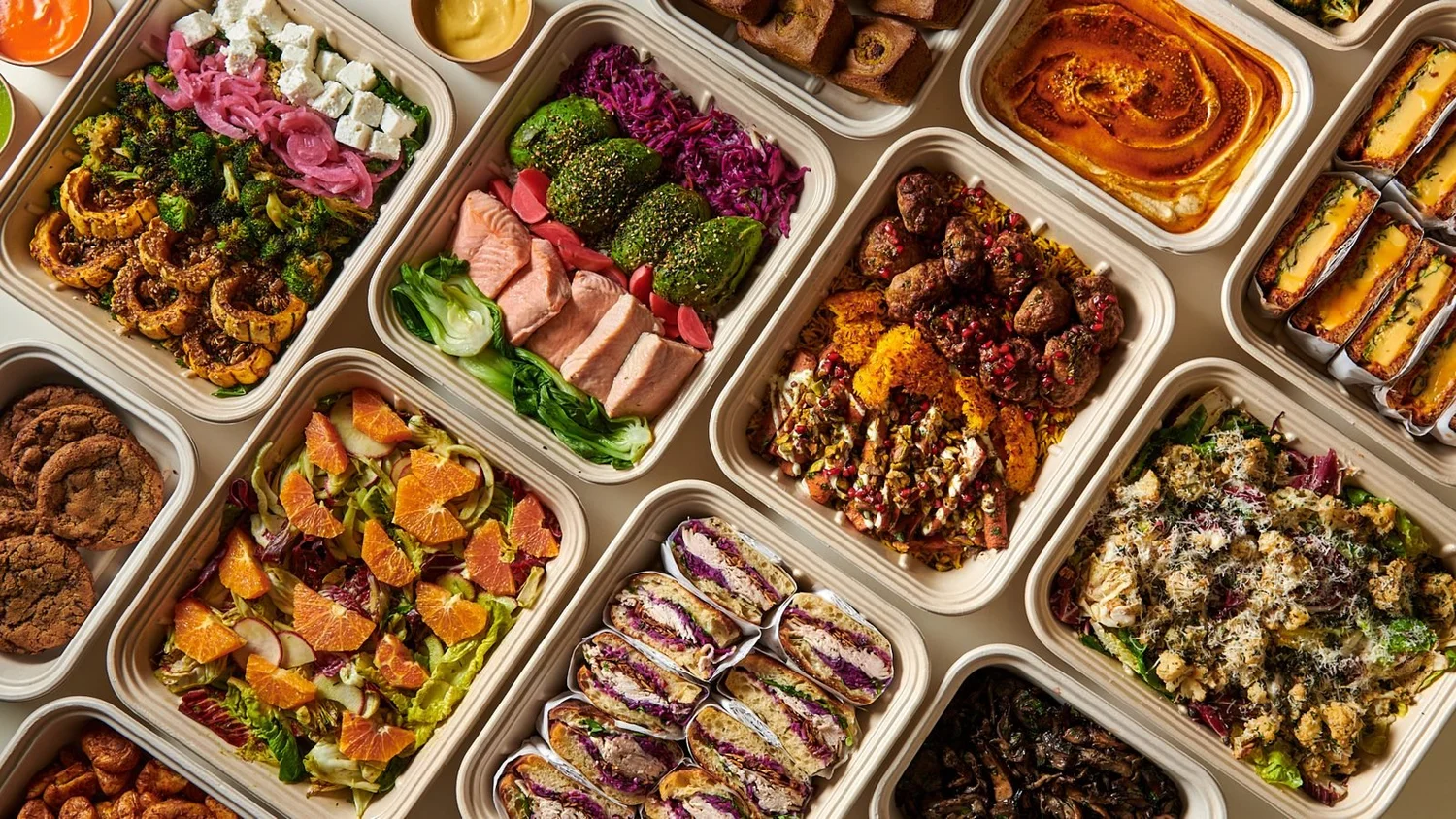 A catering spread of bowls, salads, sandwiches, hummus and cookies