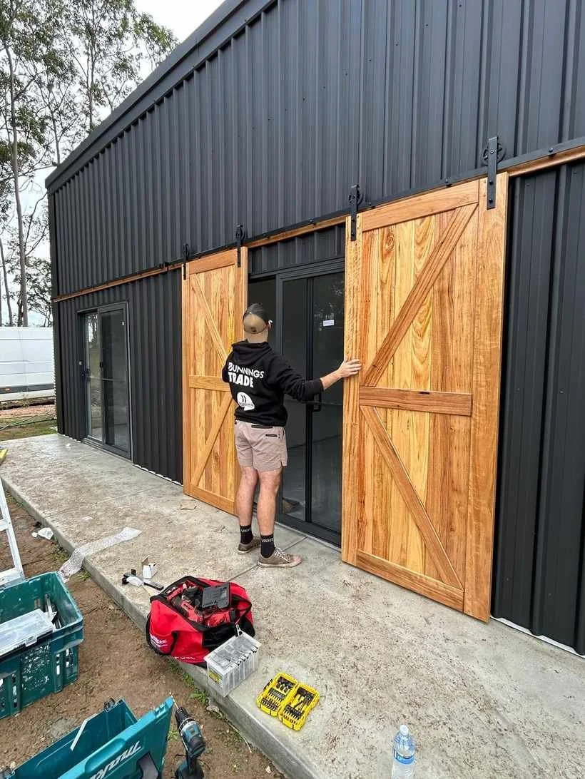 Pair of hardwood sliding barn doors being fitted to a dark shed