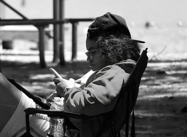 Black-and-white photograph of a person seated outdoors, looking down at a phone.