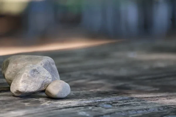 Three smooth pale rocks resting together on a weathered picnic table, photographed with a softly blurred background.