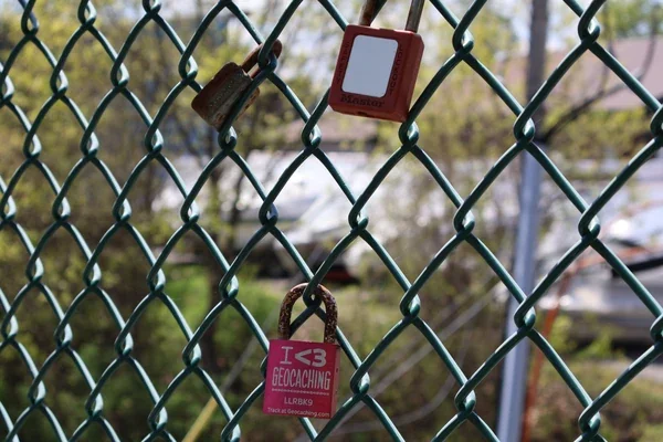 Padlocks and a red square marker hang from a green chain-link fence.