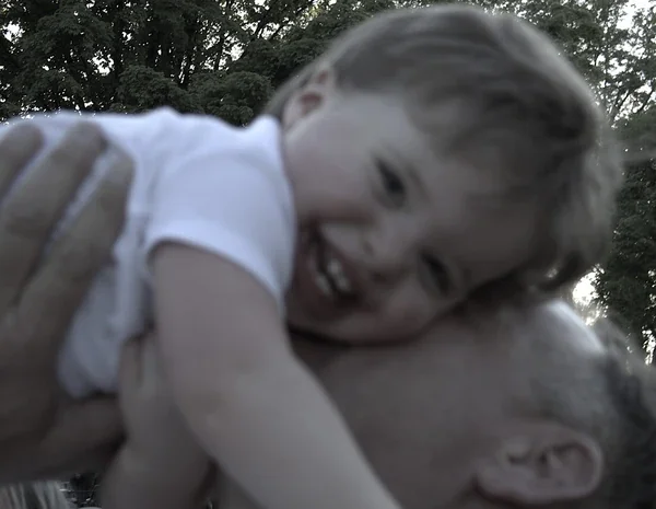 Black-and-white close-up of a smiling child held against a man’s face.