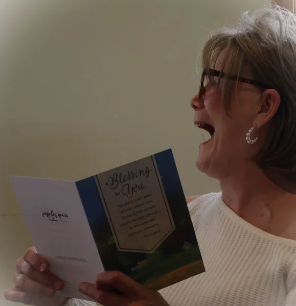 A woman wearing glasses holds an open birthday card, her mouth open in surprise.
