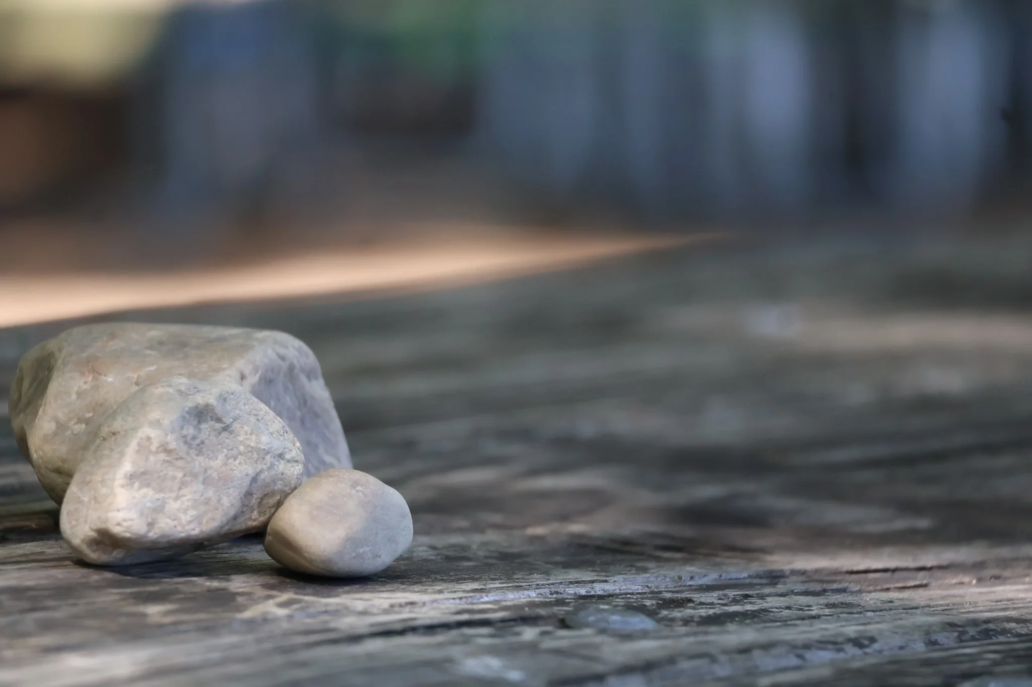 Three smooth pale rocks resting together on a weathered picnic table, photographed with a softly blurred background.