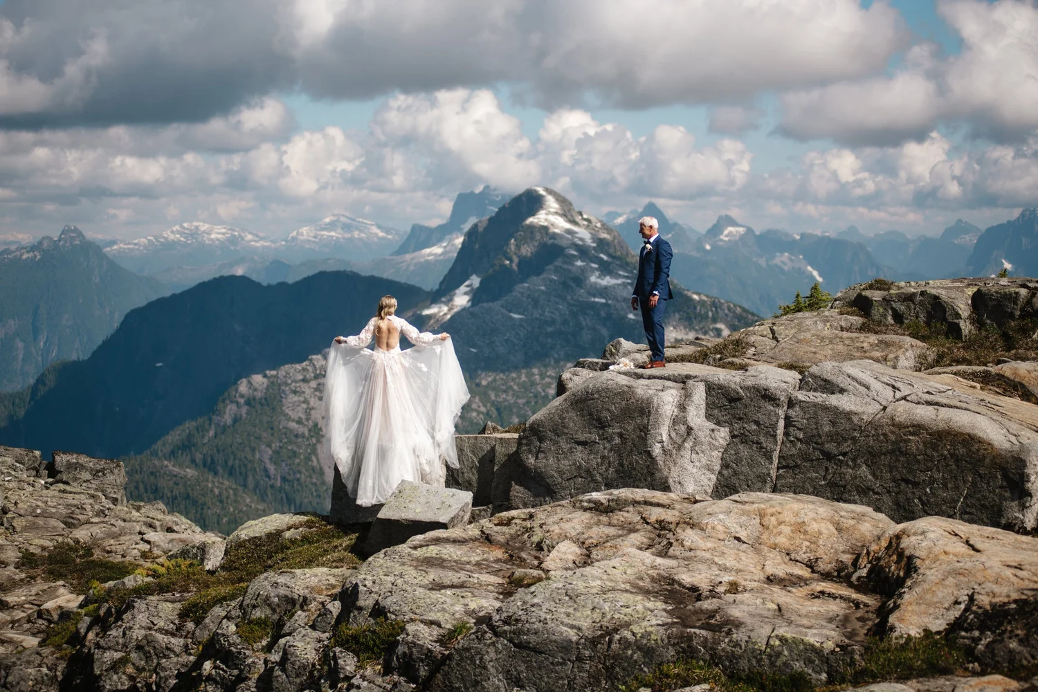A couple on a high rocky lookout over a mountain range, her veil spread across the rock