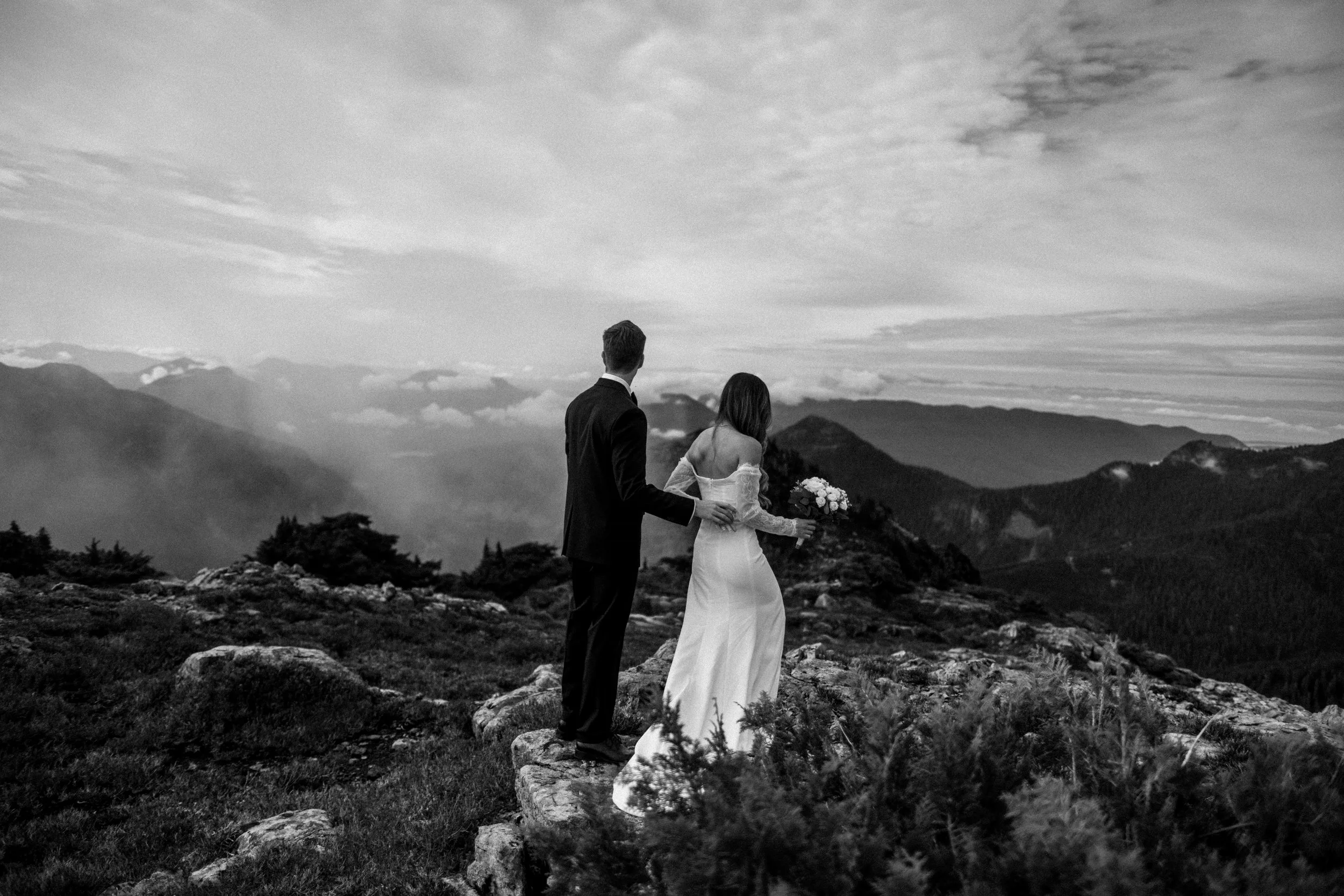 A couple standing together on a mountain ridge above the clouds, in black and white