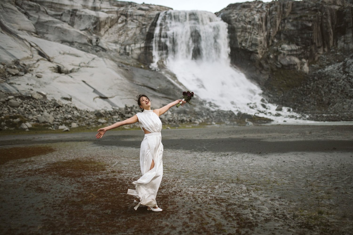 A bride with her arms outstretched in front of a waterfall on Vancouver Island
