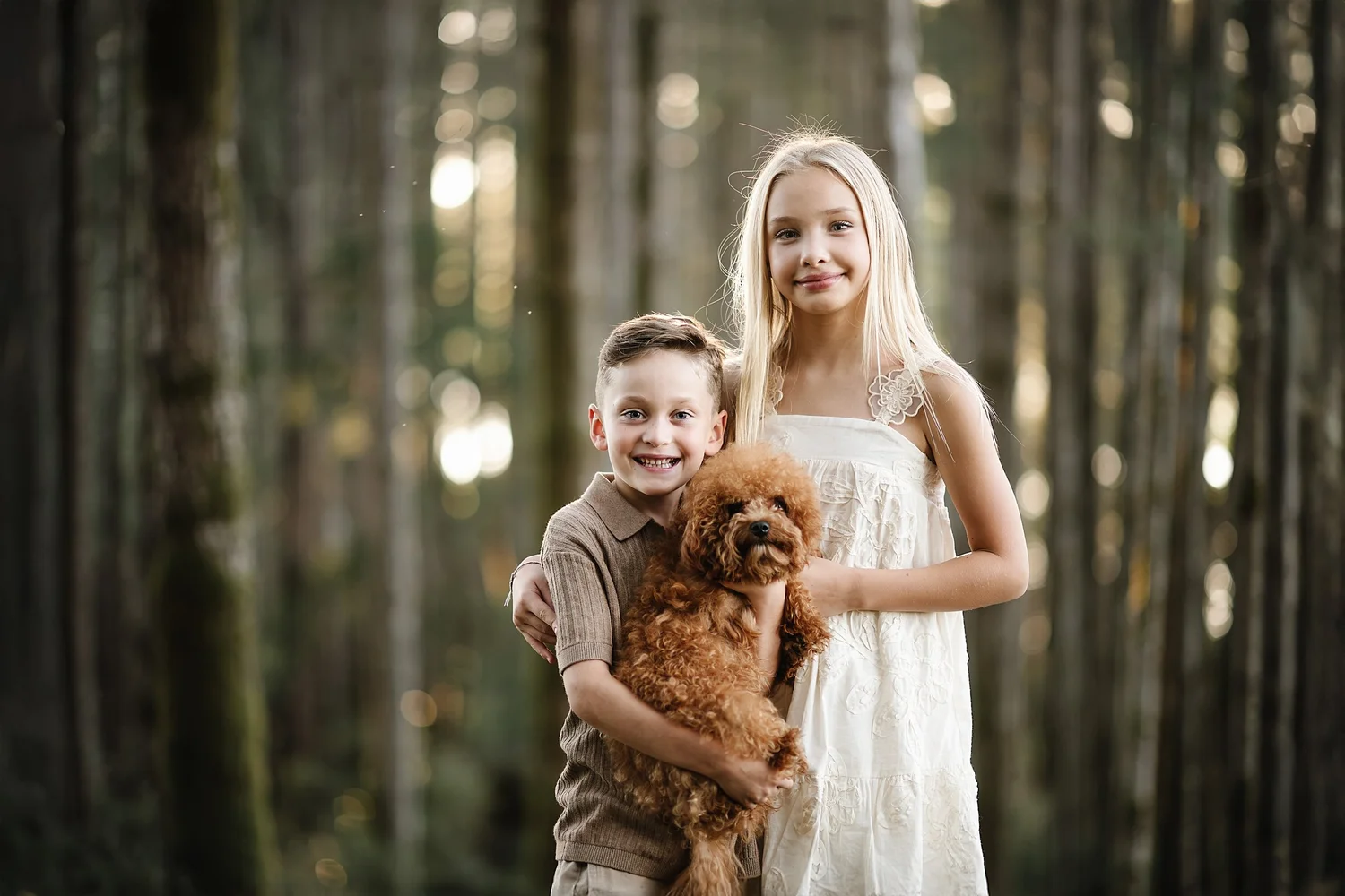 A brother and sister with their puppy in a sunlit forest